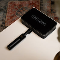 Carbon Ignis torch lighter on its black tin on a side table