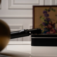 Carbon Ignis torch lighter on its tin beside a framed picture