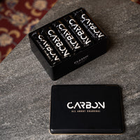 Carbon Classic charcoal rolls in an open tin on a stone surface