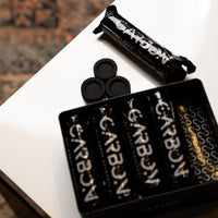 Open Carbon Classic tin with charcoal pieces on a side table