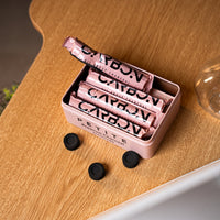 Open Carbon Petite tin with charcoal rolls on a wooden table
